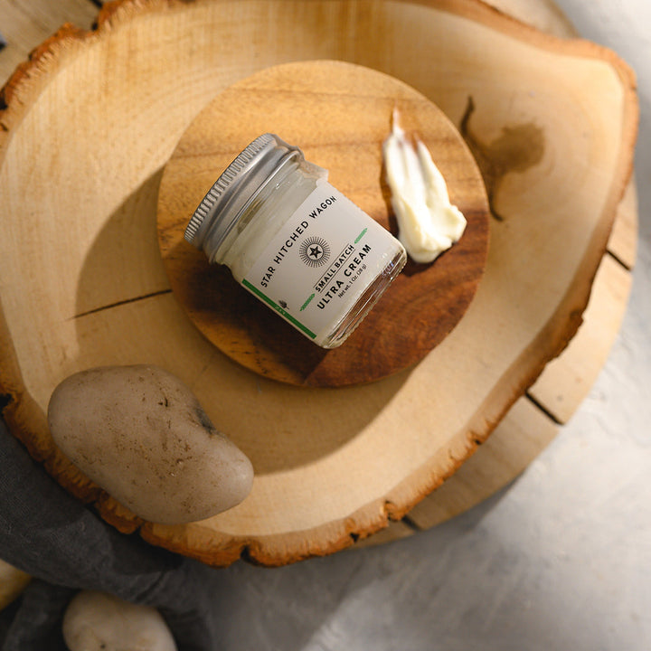 A small glass jar of Star Hitched Wagon Liz Ultra Cream lays on a round wooden slice, with a dollop of ultra cream next to jar.