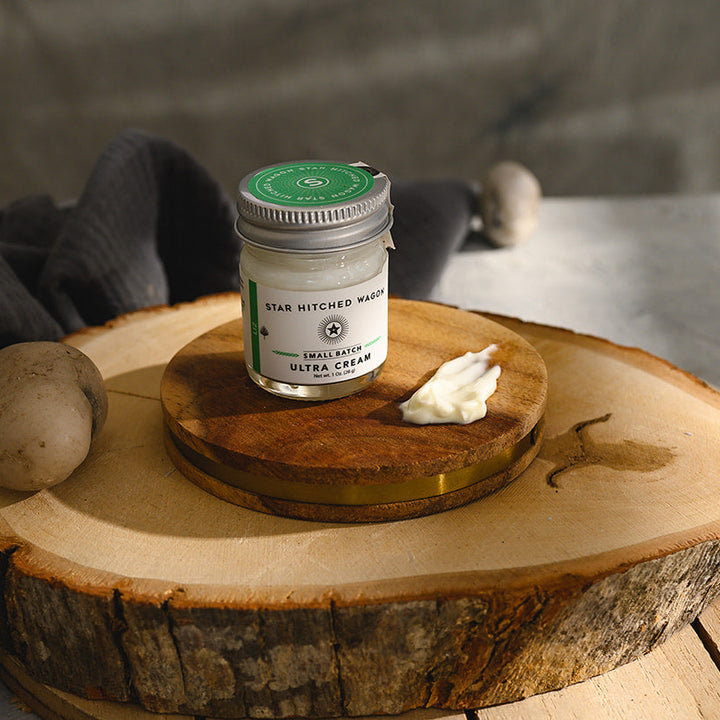 A small glass jar of Star Hitched Wagon Liz Ultra Cream sits on a round wooden slice, with a dollop of ultra cream next to jar.