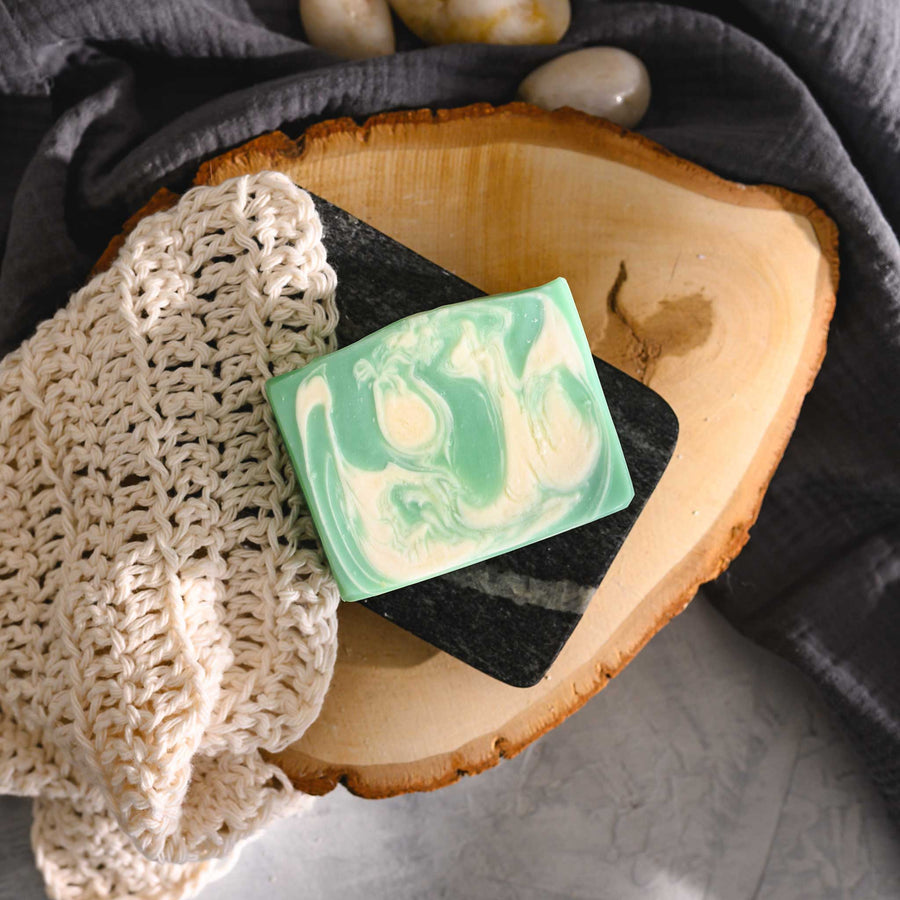 Liz essential oil soap bar with swirls of pale green and white, resting on a wooden surface with a cream colored washcloth beside it.