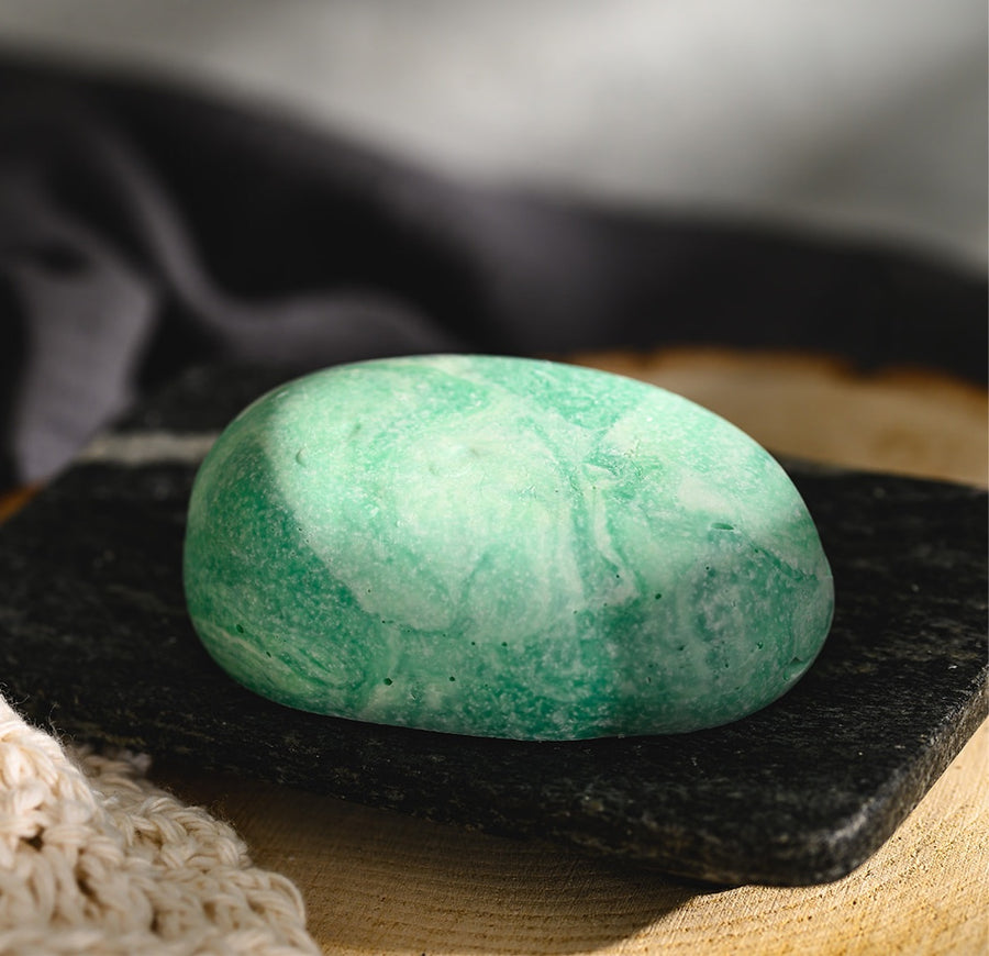 Liz River Stone Salt Soap Bar with a greenish color and a smooth texture, resting on a black stone surface.