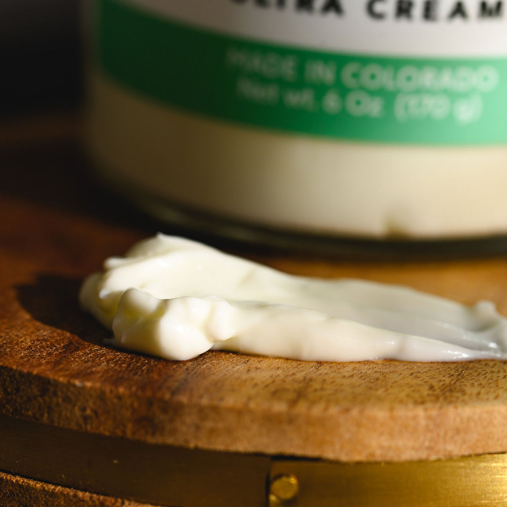 Close up of Edie Ultra Cream in front of a glass jar displayed on a wooden surface.