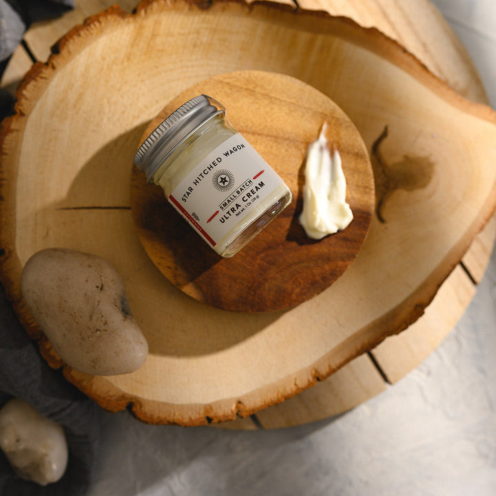 A small glass jar of Star Hitched Wagon Margo Ultra Cream lays on a round wooden slice, with a dollop of ultra cream next to jar.