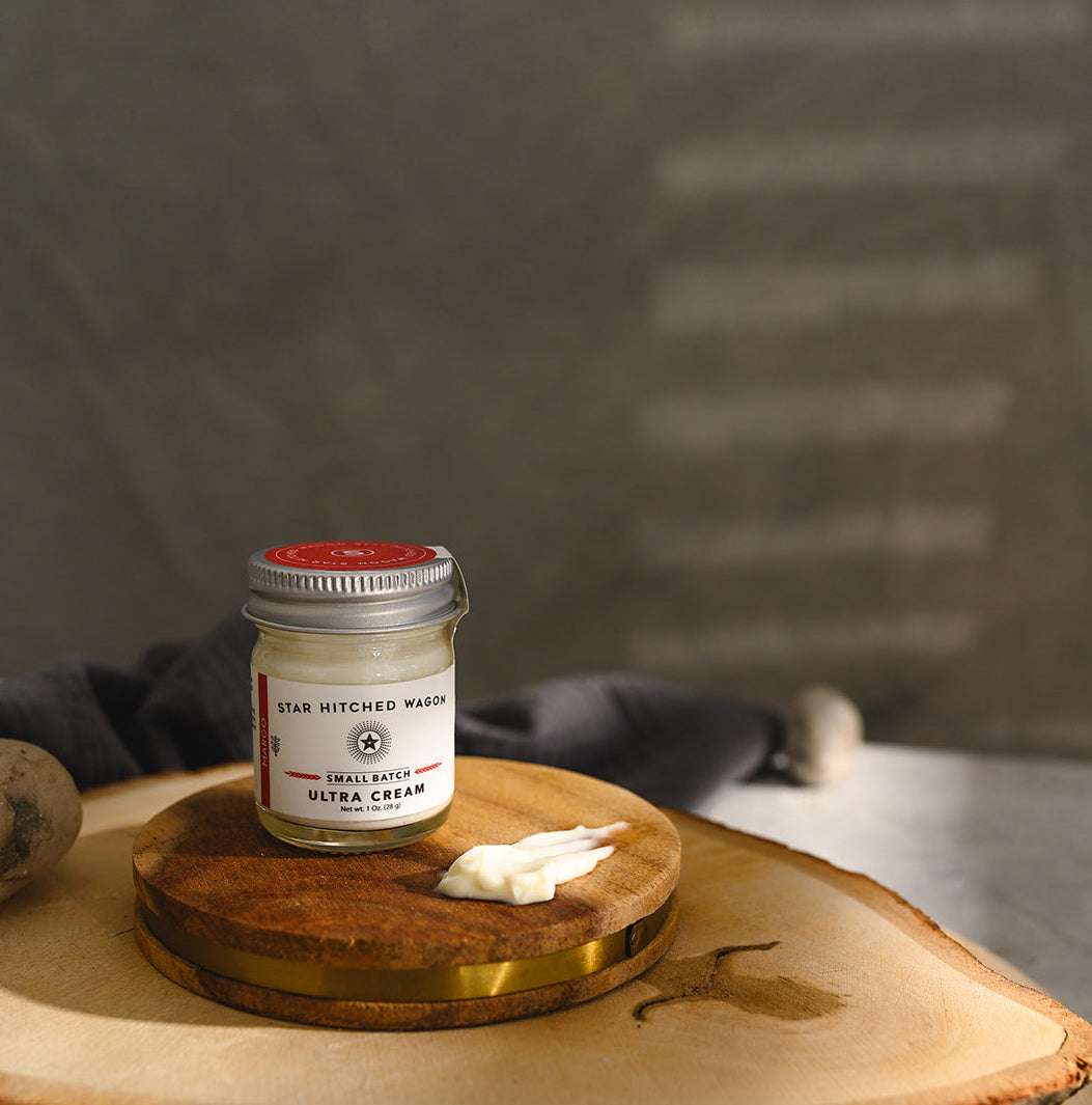 A small glass jar of Star Hitched Wagon Margo Ultra Cream sits on a round wooden slice, with a dollop of ultra cream next to jar.