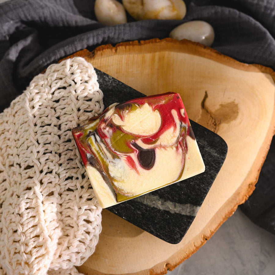 Margo essential oil soap bar with swirls of red, green, brown, and cream, placed on a wooden surface with a knit washcloth beside it.