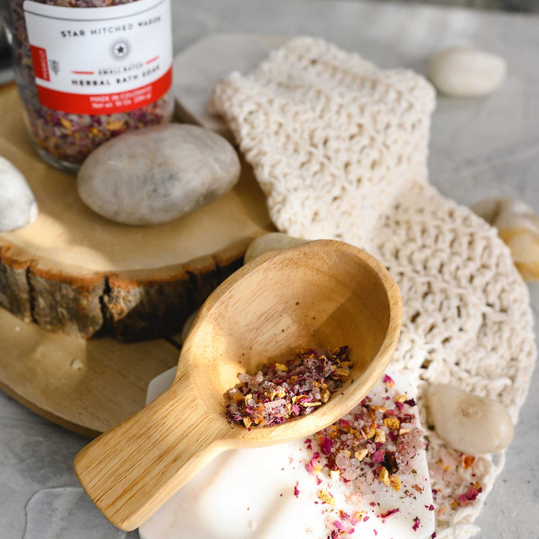 Margo herbal bath soak in a wooden scoop placed on a knit washcloth next to a wooden slab and small river stones.