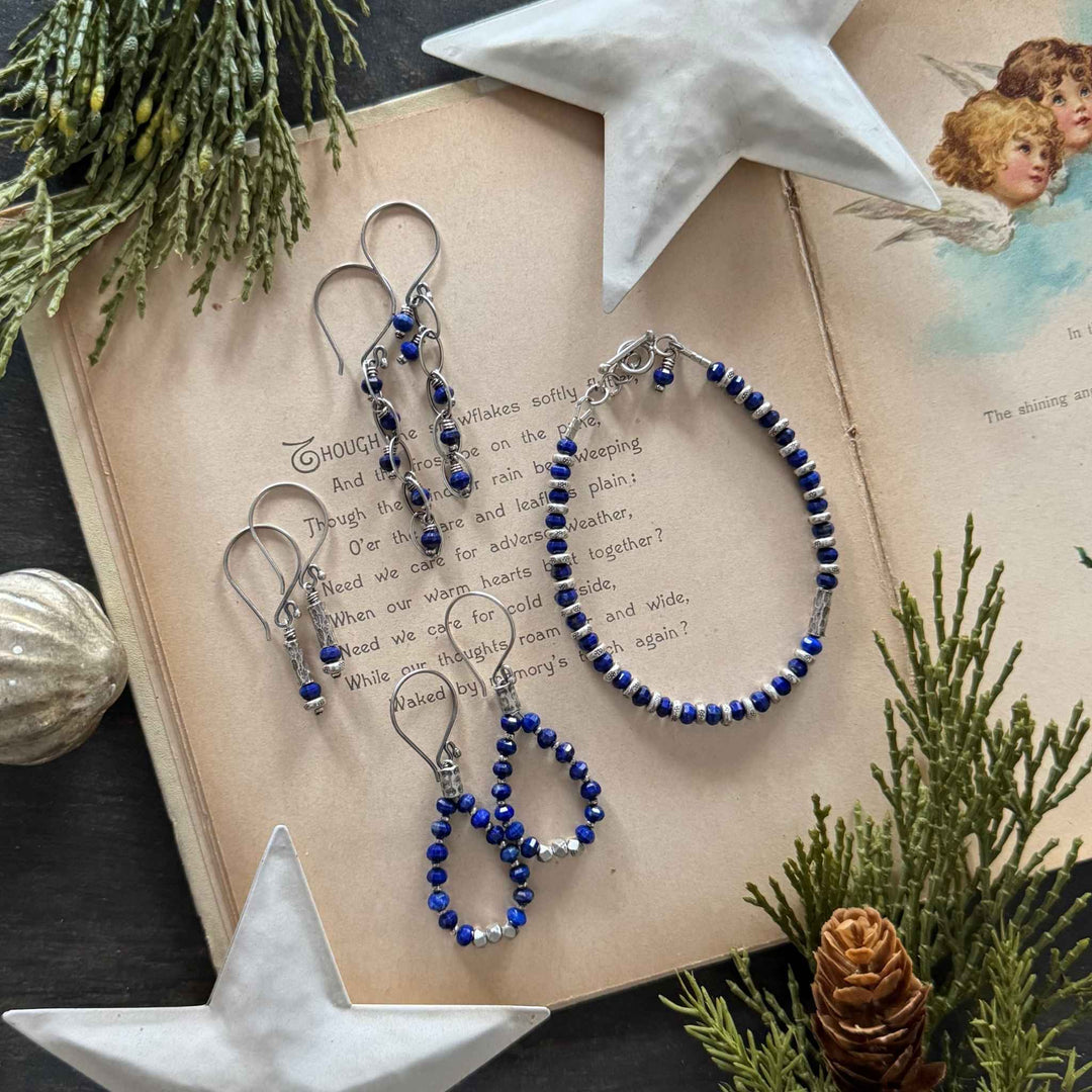 Lapis bracelet and three earring styles with sterling and Thai silver accents displayed on a vintage holiday book with winter greenery and stars.