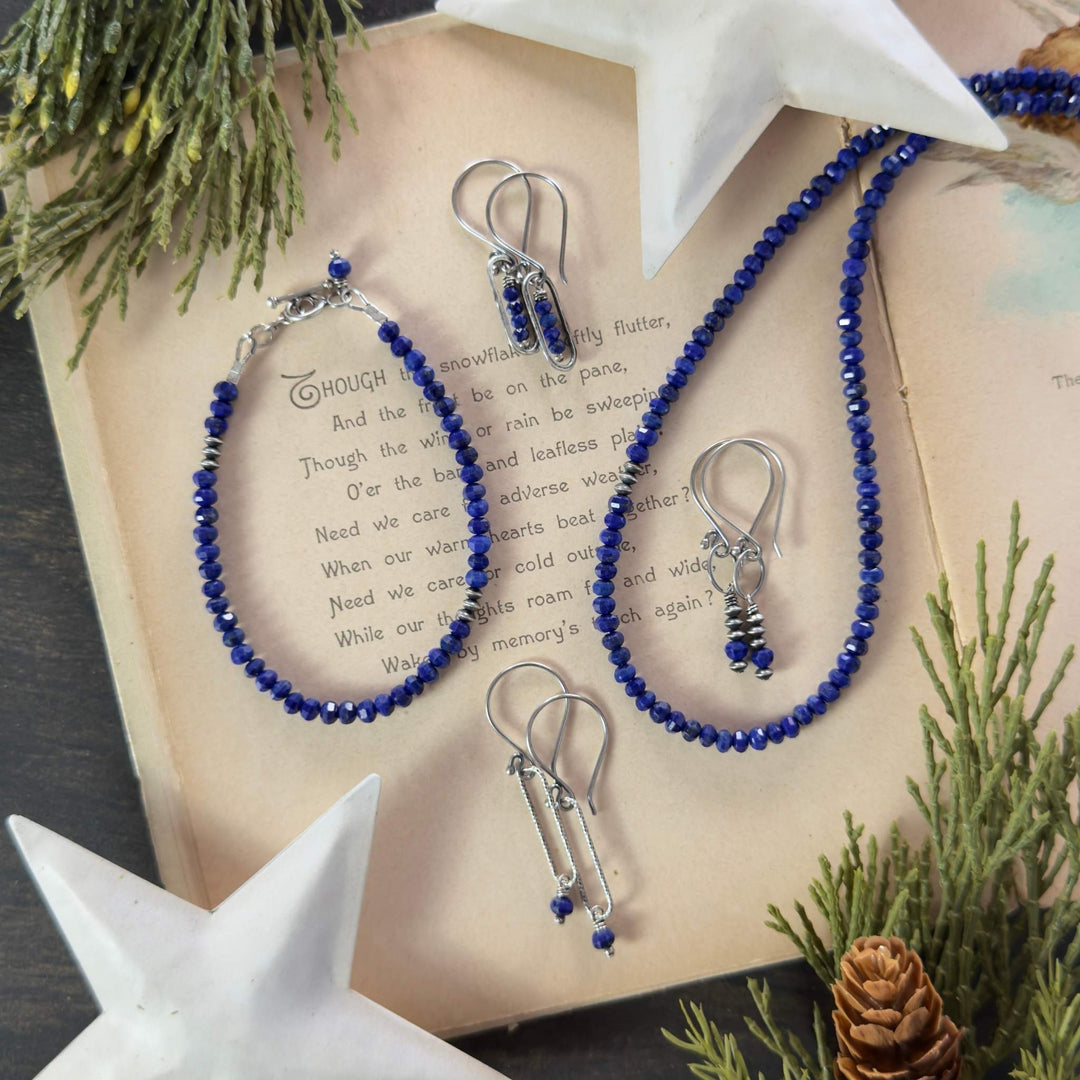 Midnight Lapis necklace, bracelet, and two earring styles with oxidized and sterling silver accents displayed on a vintage holiday book with greenery and stars.