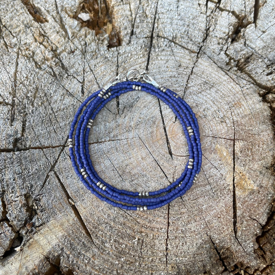 Navy blue seed bead wrap bracelet with Thai silver rondelles and a Bali silver toggle clasp displayed coiled on a stone background.