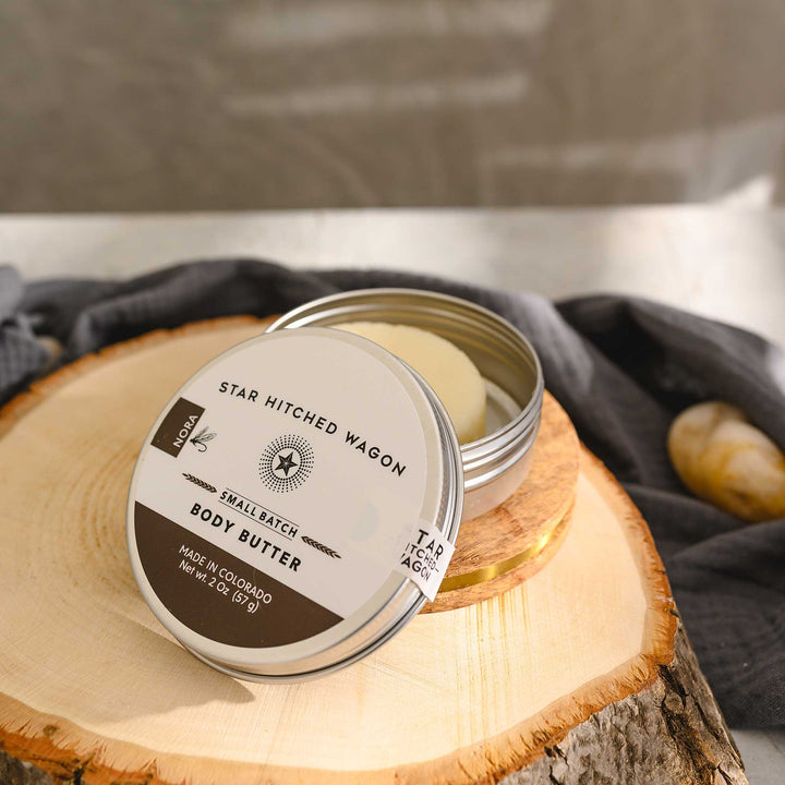 Nora body butter moisturizer in reusable tin, handcrafted with all natural oils and butters. Softly scented with orange, coriander, and vanilla.