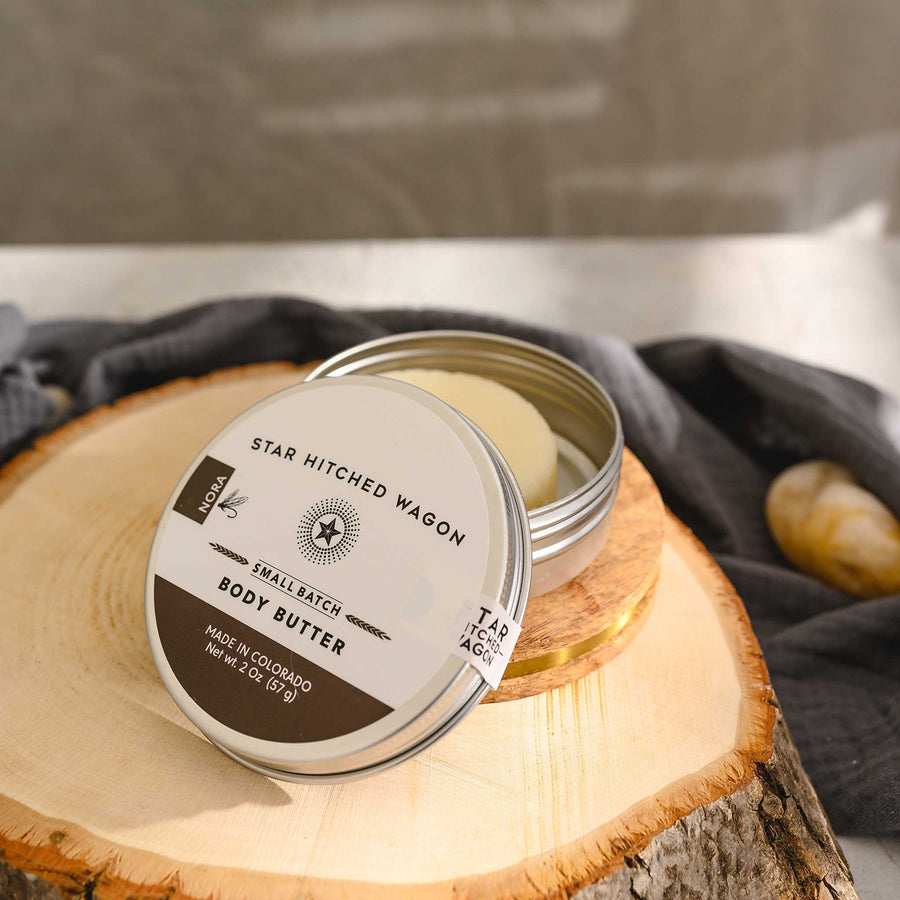 Nora body butter moisturizer in reusable tin, handcrafted with all natural oils and butters. Softly scented with orange, coriander, and vanilla.