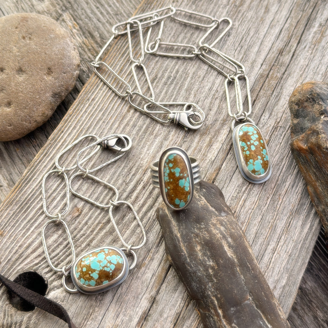 Number 8 Turquoise Ring, Necklace and Bracelet on wooden background with rocks and leather lace.