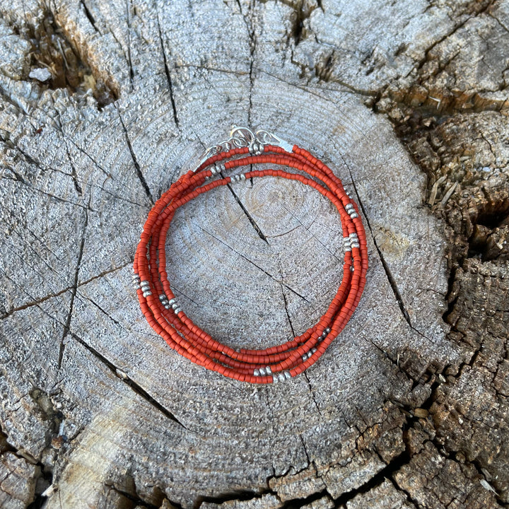 Orange seed bead wrap bracelet on a textured wooden background.