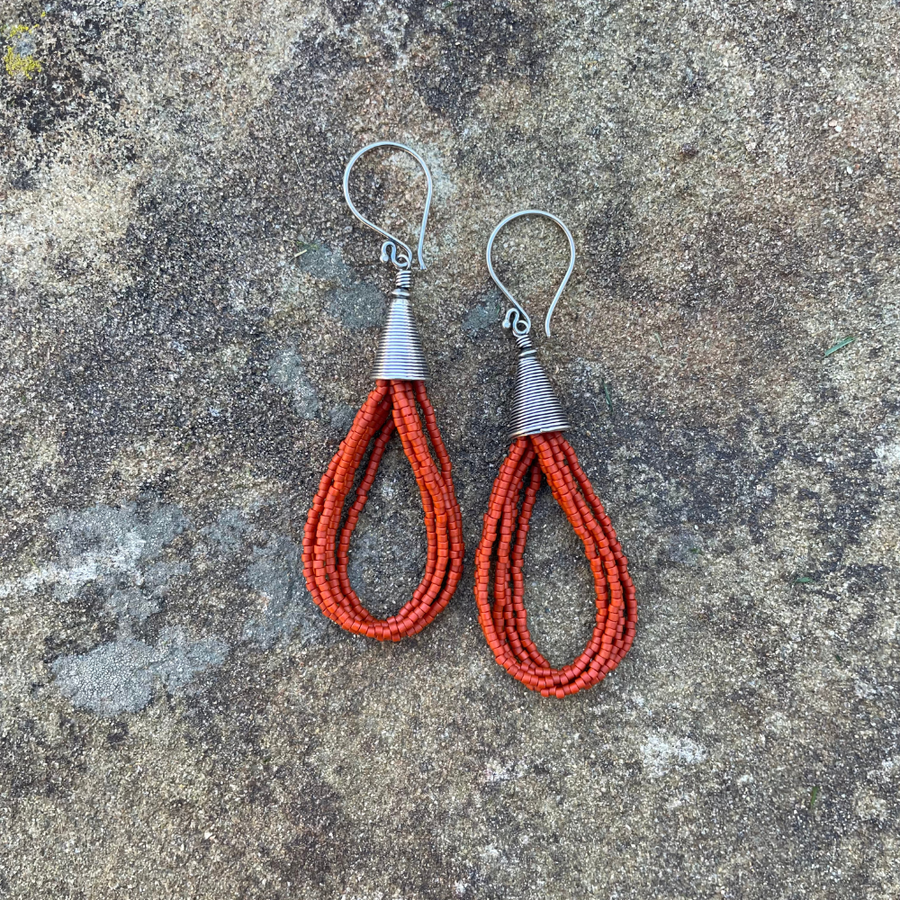Orange seed bead earrings with sterling silver ear wires and Bali-style cone tops displayed on a textured stone background.