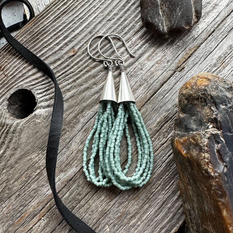 A pair of pale turquoise seed bead earrings in loop style with silver accents, displayed on a wooden surface.