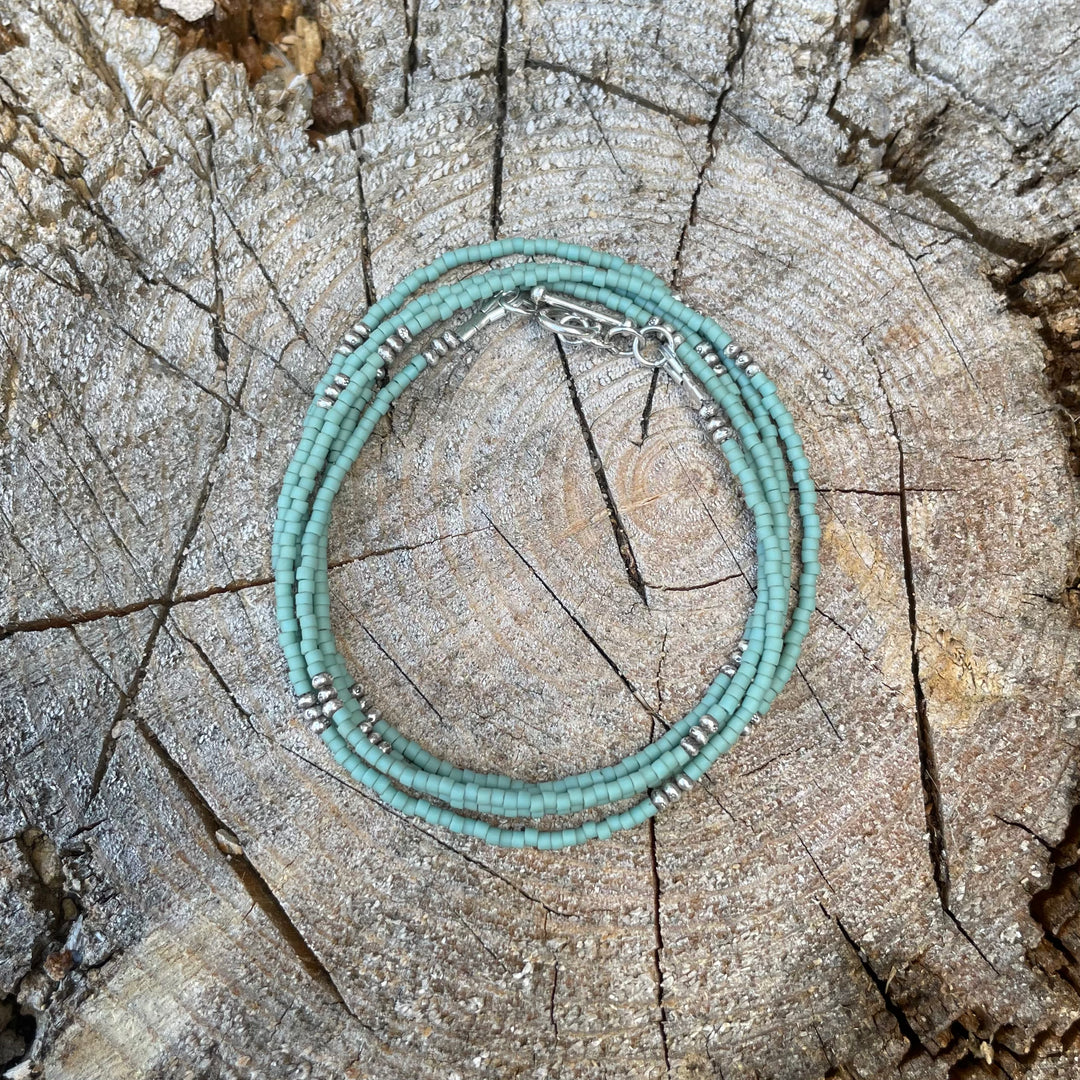 Matte pale turquoise seed bead wrap bracelet with Thai silver rondelles and a Bali silver toggle clasp displayed coiled on a wood background.