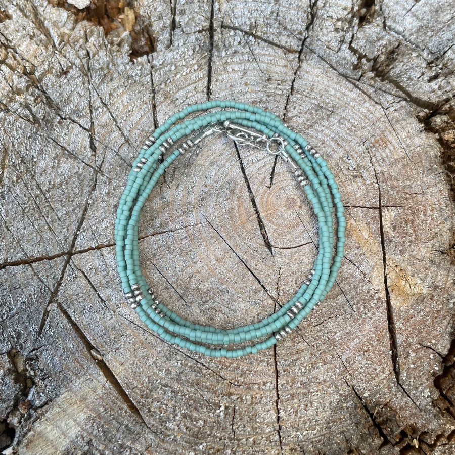 Matte pale turquoise seed bead wrap bracelet with Thai silver rondelles and a Bali silver toggle clasp displayed coiled on a wood background.