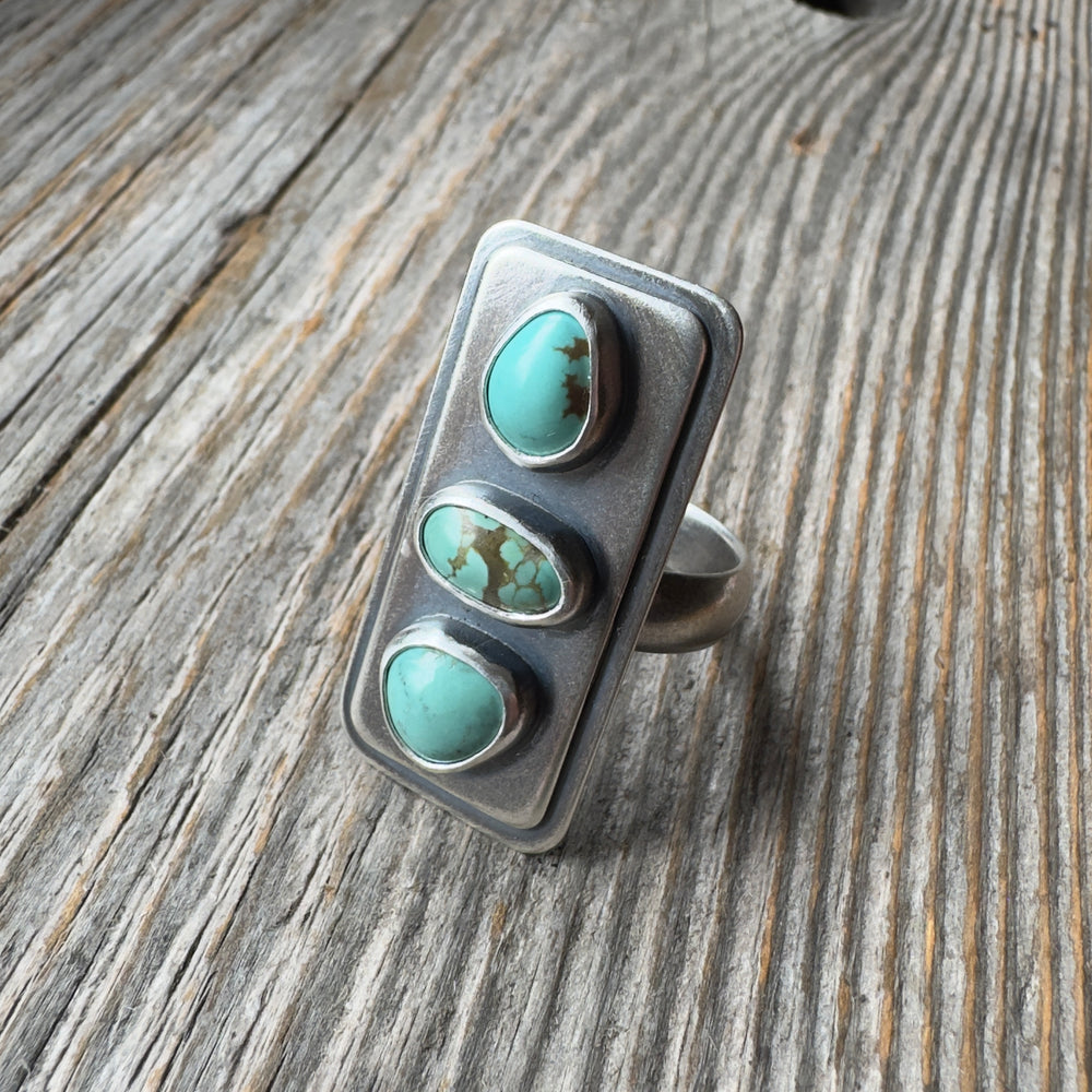 Three stone #8 turquoise sterling silver statement ring with brushed oxidized finish, size 9 on wood background.