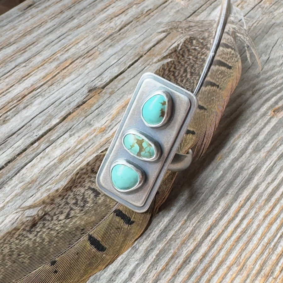 Three stone #8 turquoise sterling silver statement ring with brushed oxidized finish, size 9 on wood background with feather.