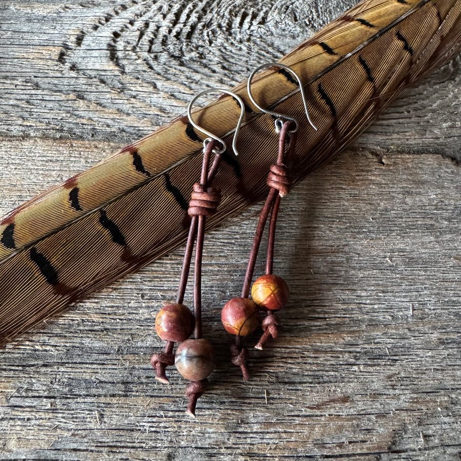 Earrings with jasper and leather on a wooden surface with feather.