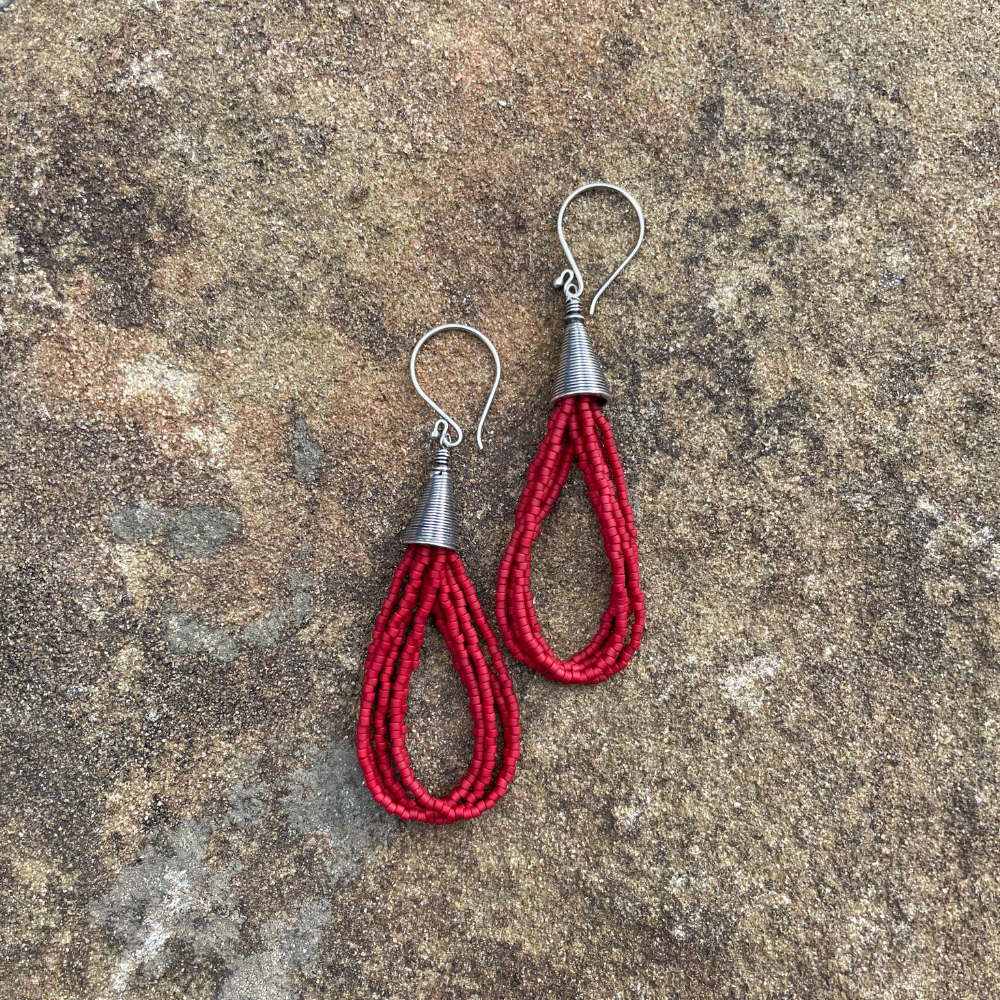Red seed bead earrings with sterling silver ear wires and Bali-style cone tops displayed on a textured stone background.