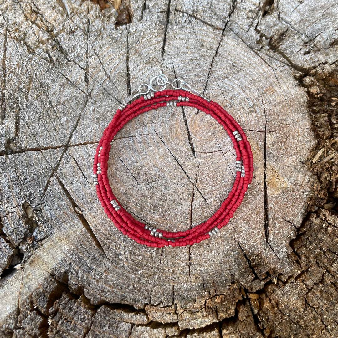Matte red seed bead wrap bracelet with Thai silver rondelles and a Bali silver toggle clasp displayed coiled on a wooden background.