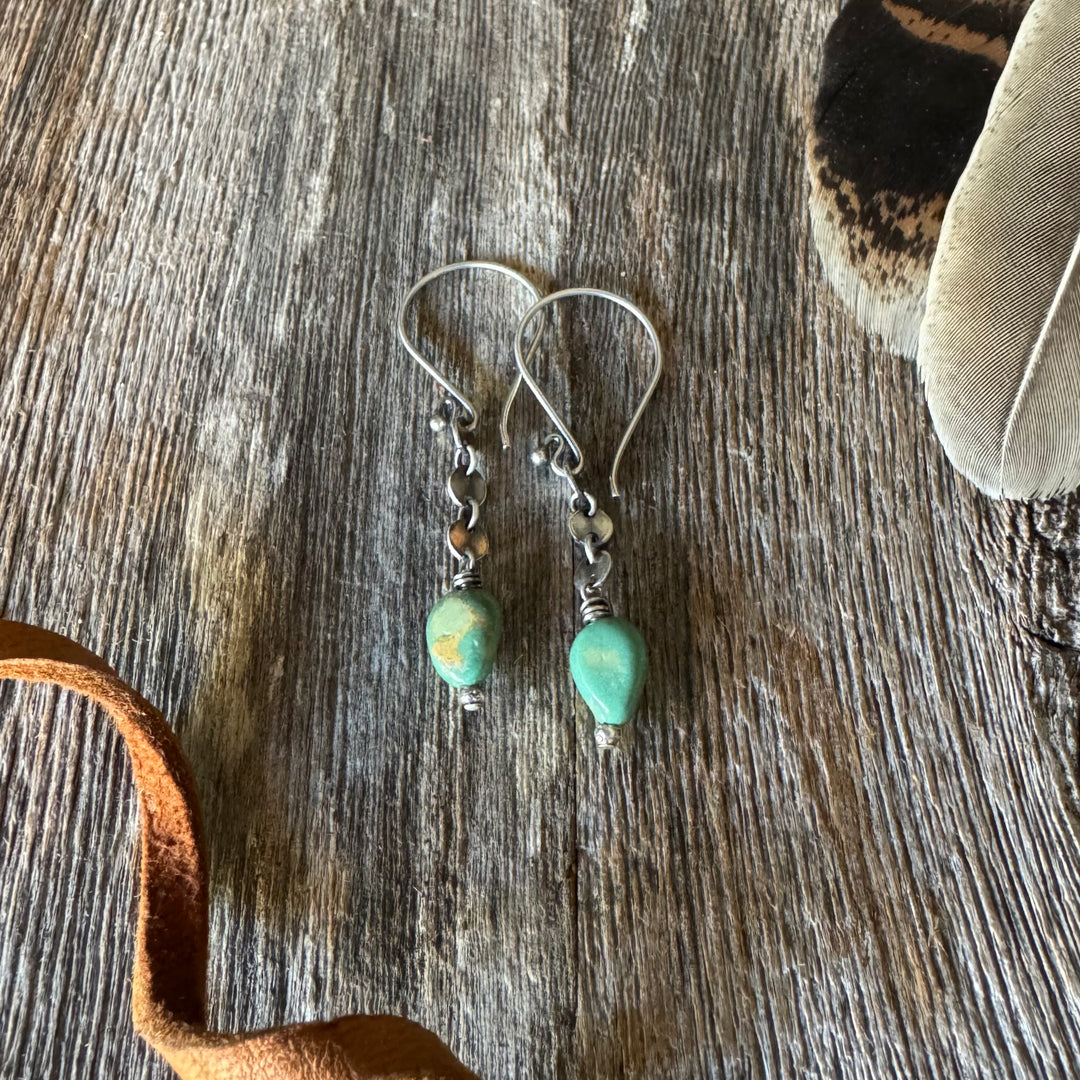 Elisa turquoise nugget and sequin chain earrings on a wooden surface with feather and leather lace.