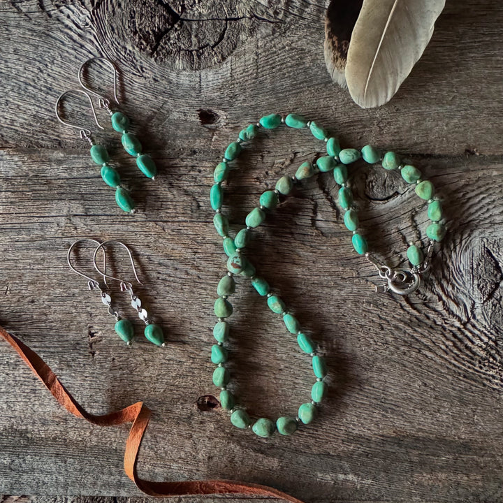 Elisa turquoise nugget necklace and earring duo on a wooden surface with feather and leather lace.