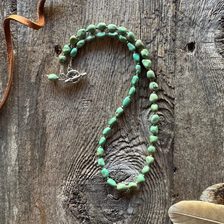 Elisa turquoise nugget necklace on a wooden surface with a feather and brown leather lace.