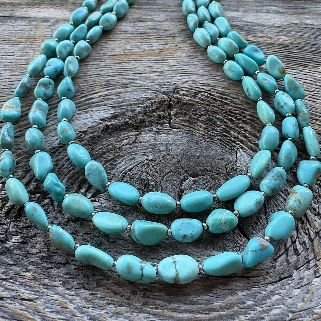 Close up of three turquoise beaded necklaces on a rustic, weathered wood surface.
