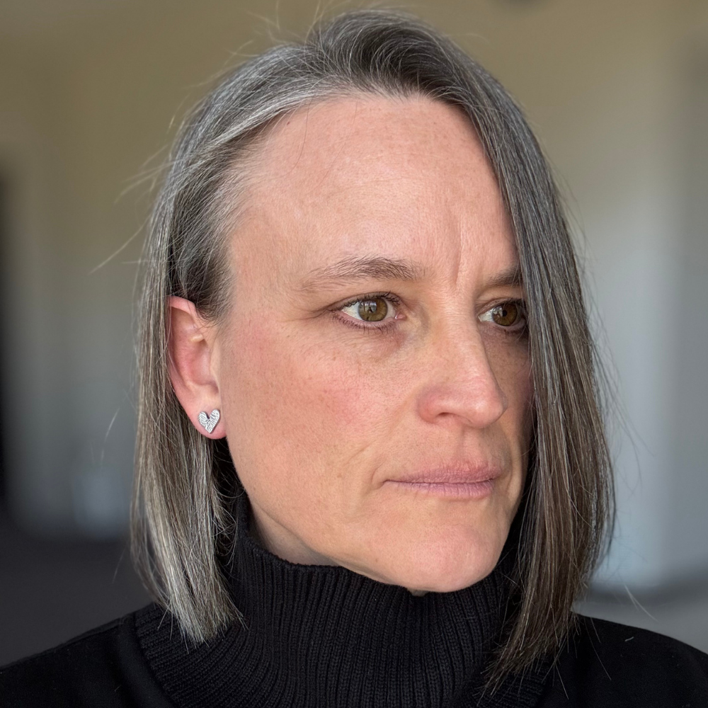 Woman with dark hair wearing a black turtleneck sweater and sterling silver feather textured post earrings against a blurred background.