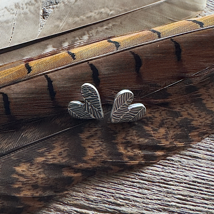 Sterling Silver feather textured heart post earrings on feather background.