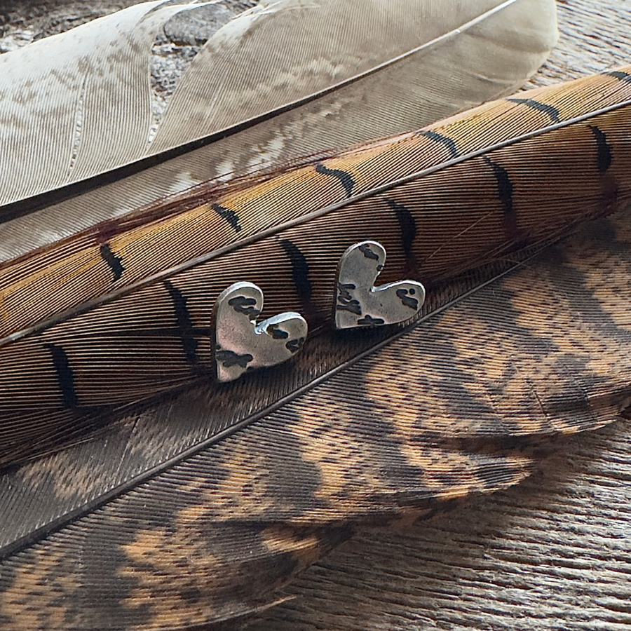 Sterling silver script embossed heart post earrings on a feather background.