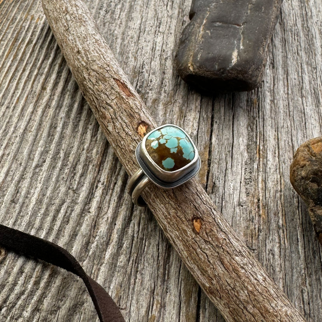 The Drift Ring — Chunky Turquoise Ring in Sterling Silver on a wooden surface with rocks and leather lace