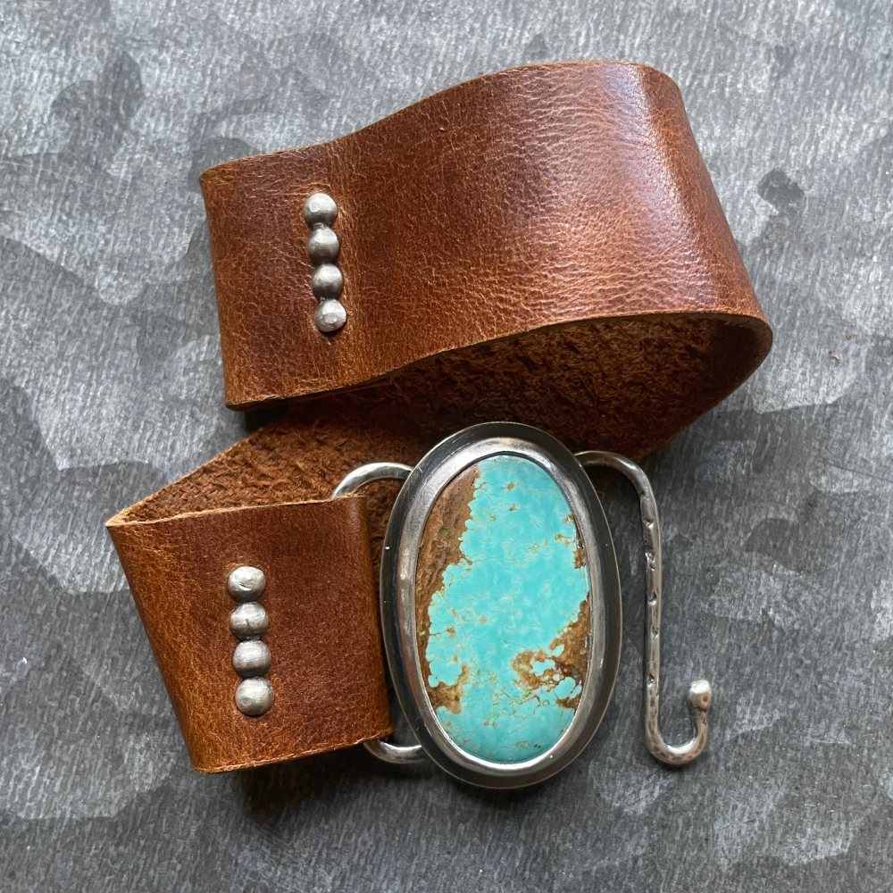 Brown leather bracelet with turquoise stone and silver accents on a gray background