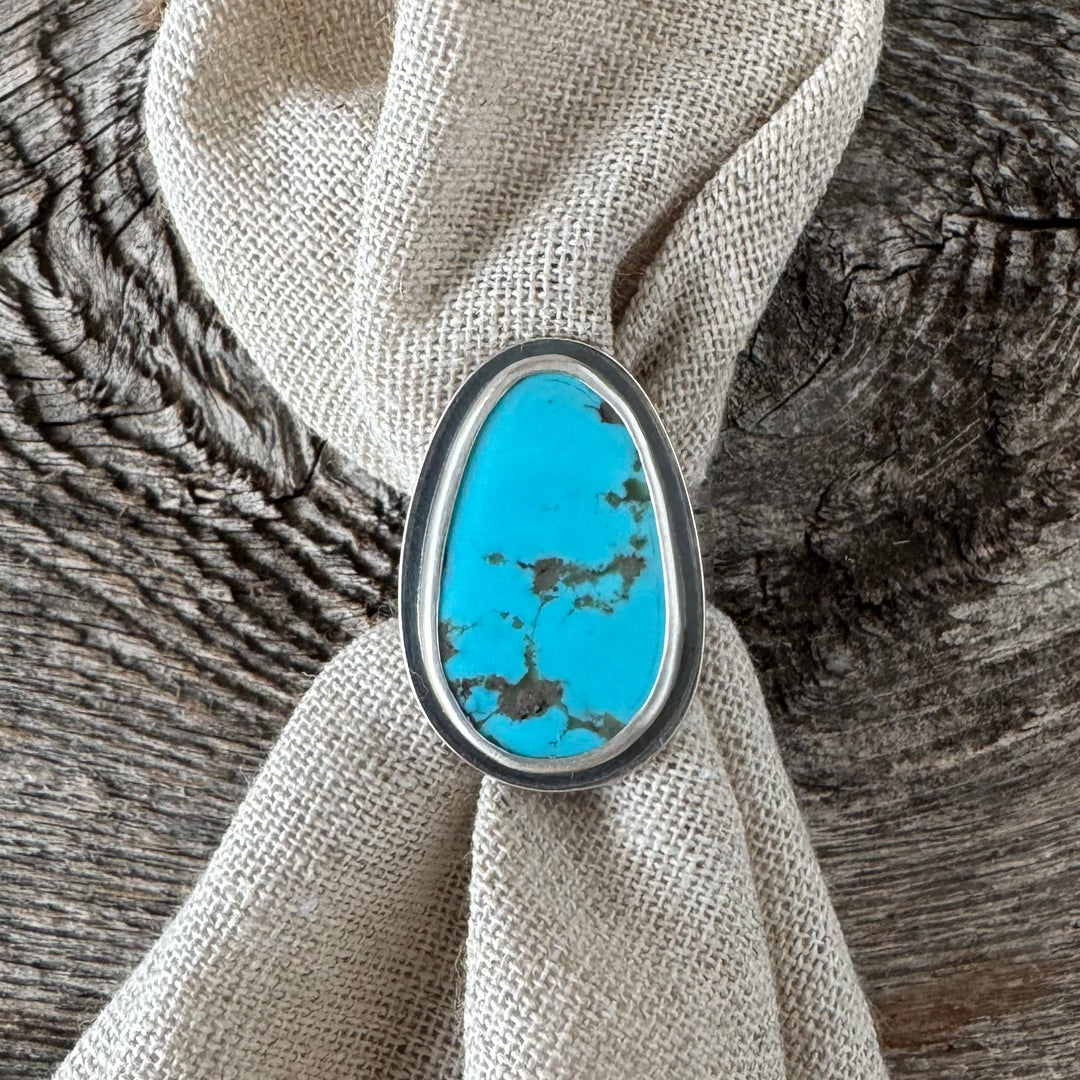 A sterling silver and turquoise stacker ring with a bold design, displayed on a textured background.