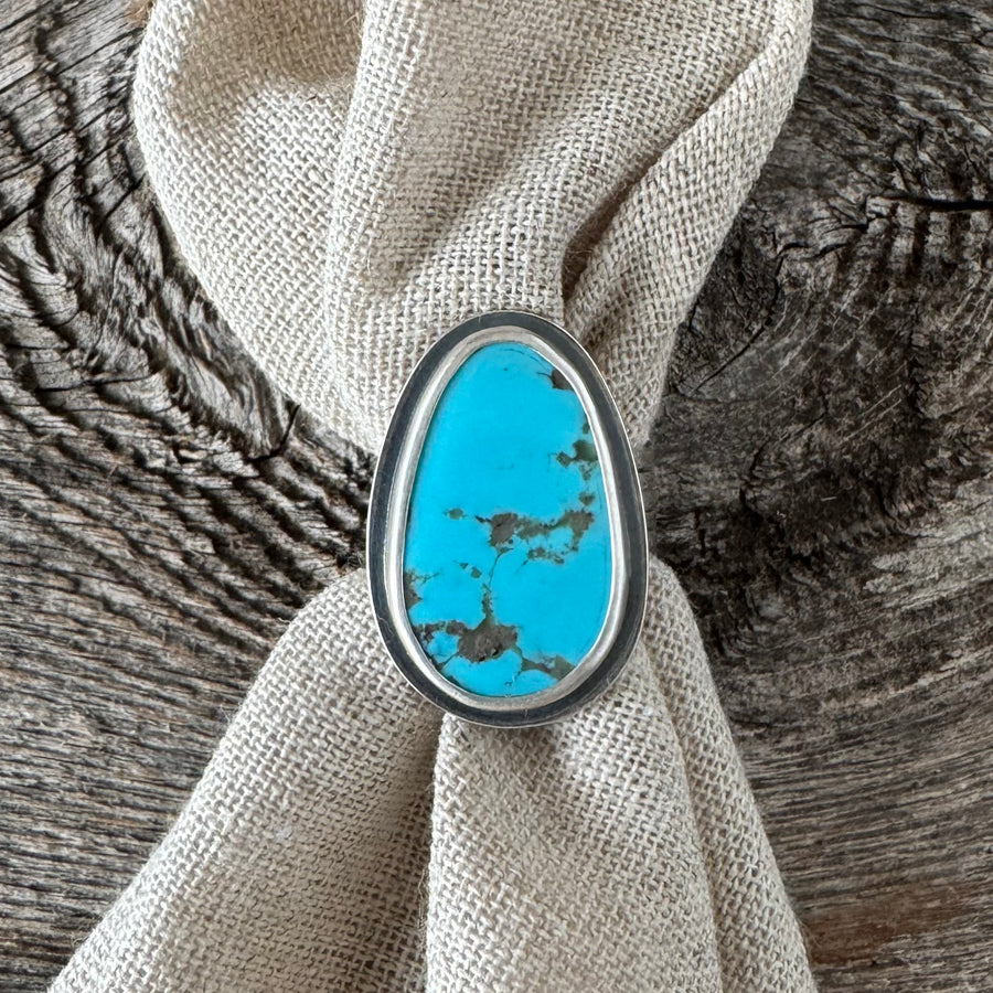 A sterling silver and turquoise stacker ring with a bold design, displayed on a textured background.