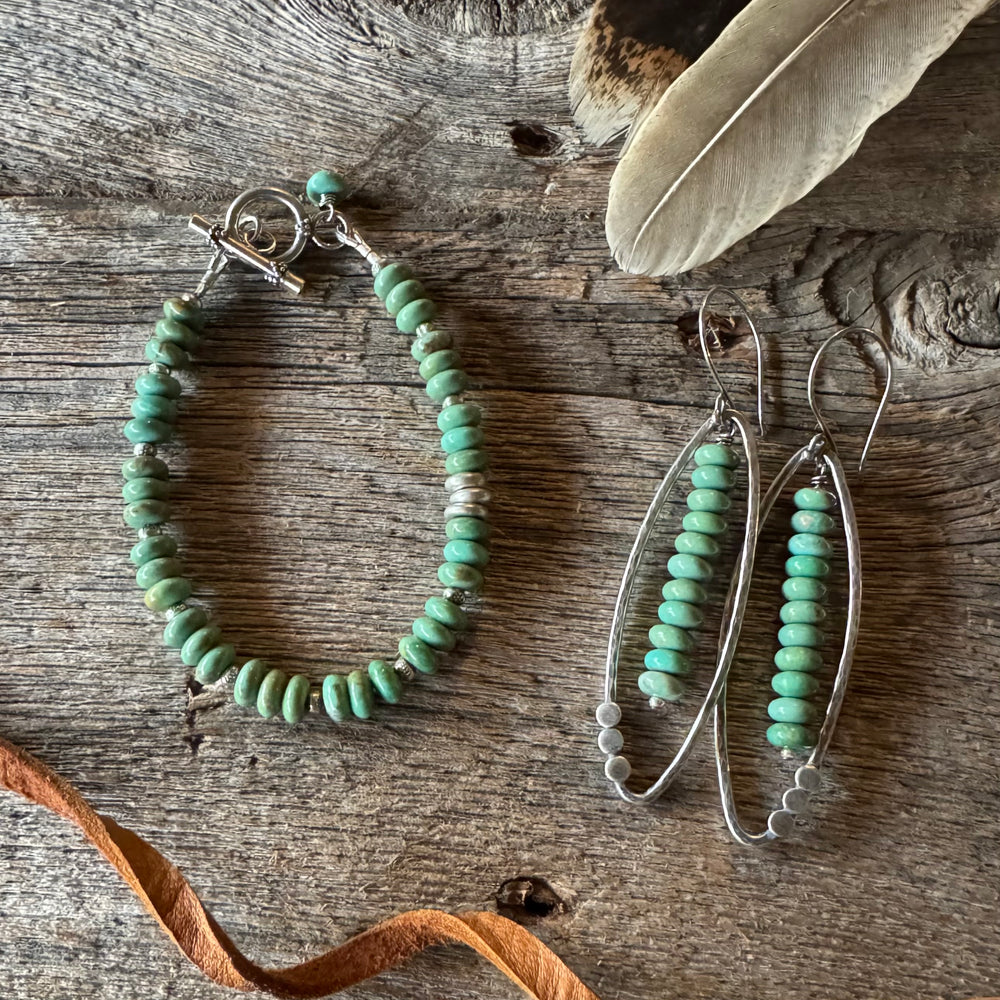 Turquoise beaded bracelet and earrings on a wooden surface with a feather and leather lace.