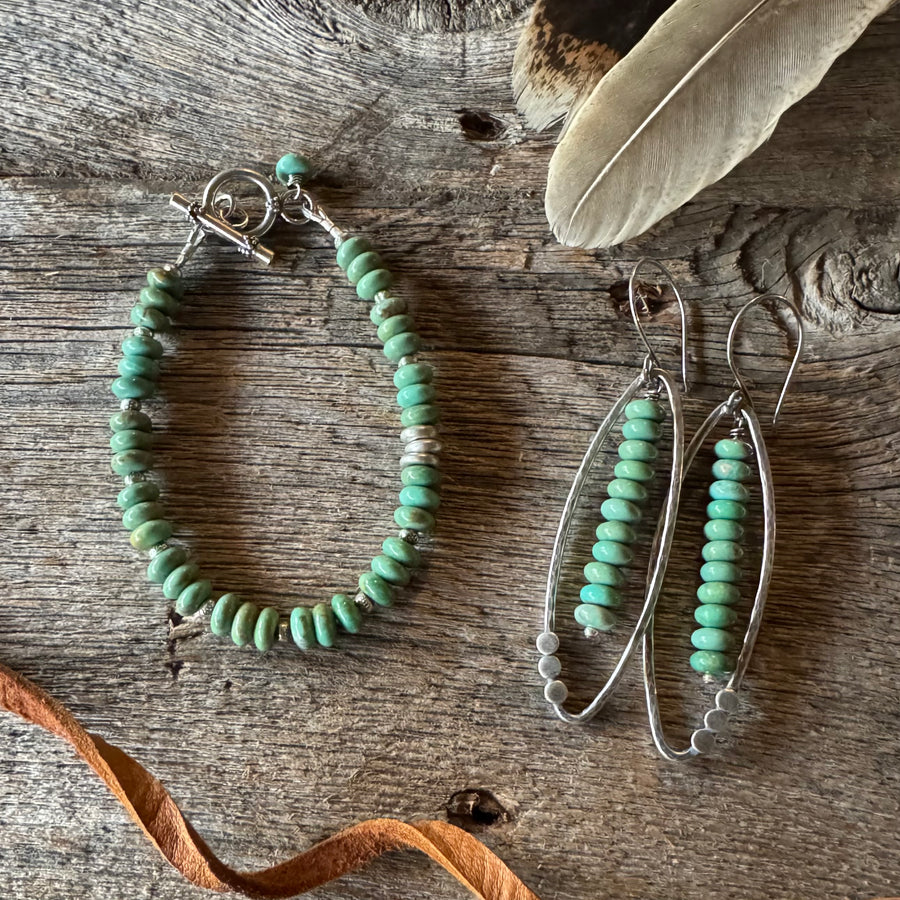 Turquoise beaded bracelet and earrings on a wooden surface with a feather and leather lace.