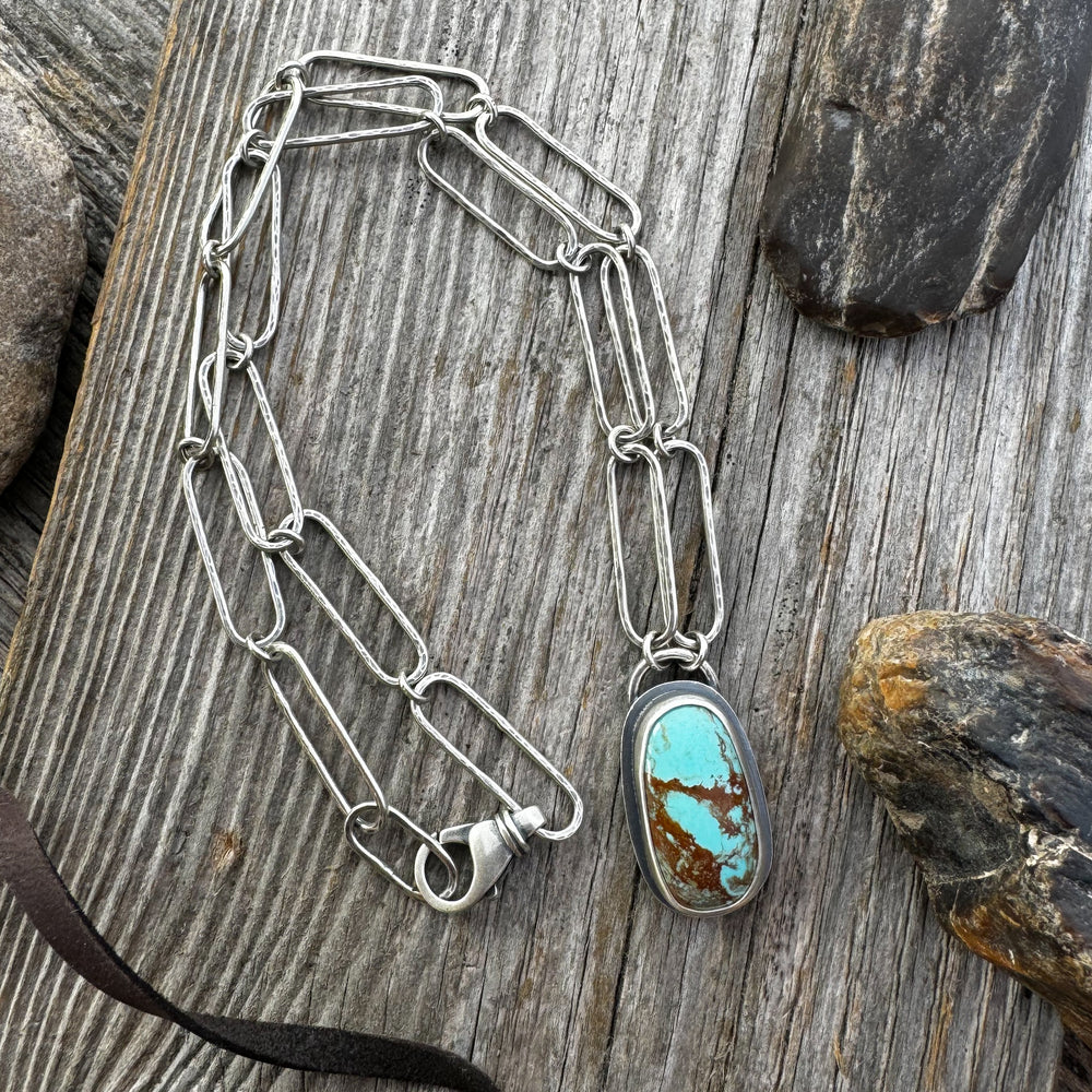 Sterling Silver and Turquoise Necklace with rocks and leather on wood surface.