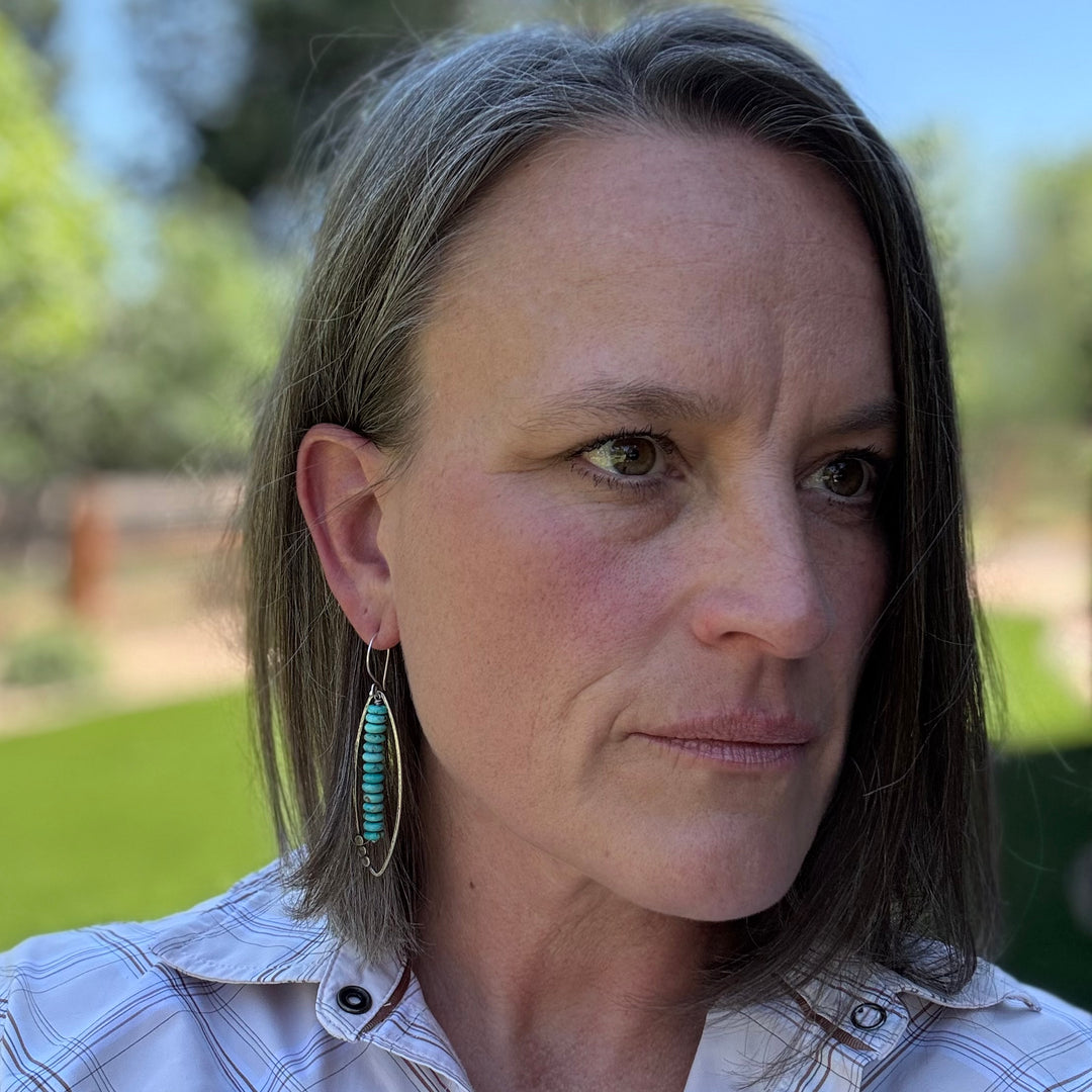 Long sterling silver and Kingman turquoise earring with open leaf and stacked turquoise rondelle design, displayed on a woman - the maker of the earrings.