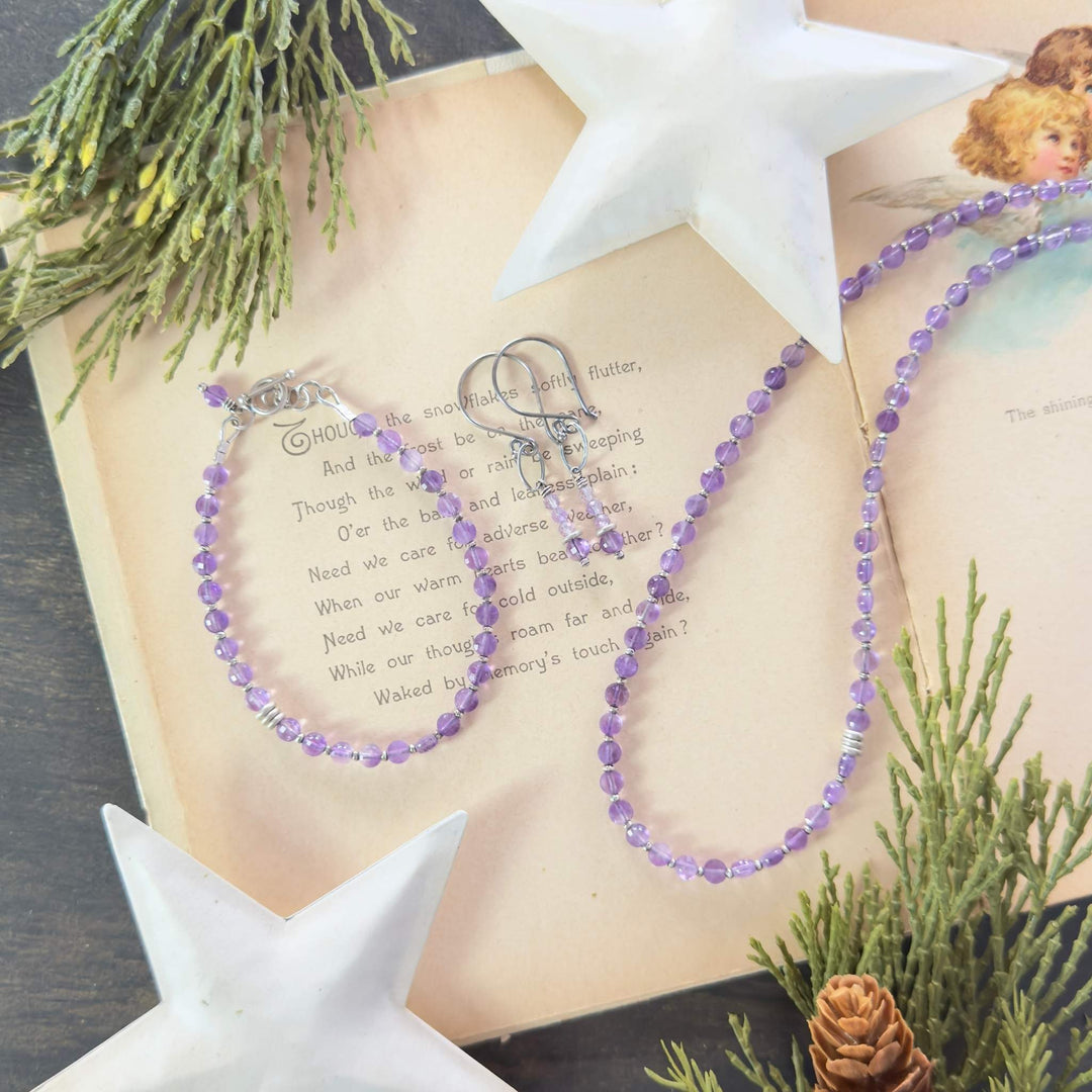 Amethyst necklace, bracelet, and earrings with Thai silver accents displayed on a vintage holiday book with greenery and white star decor.