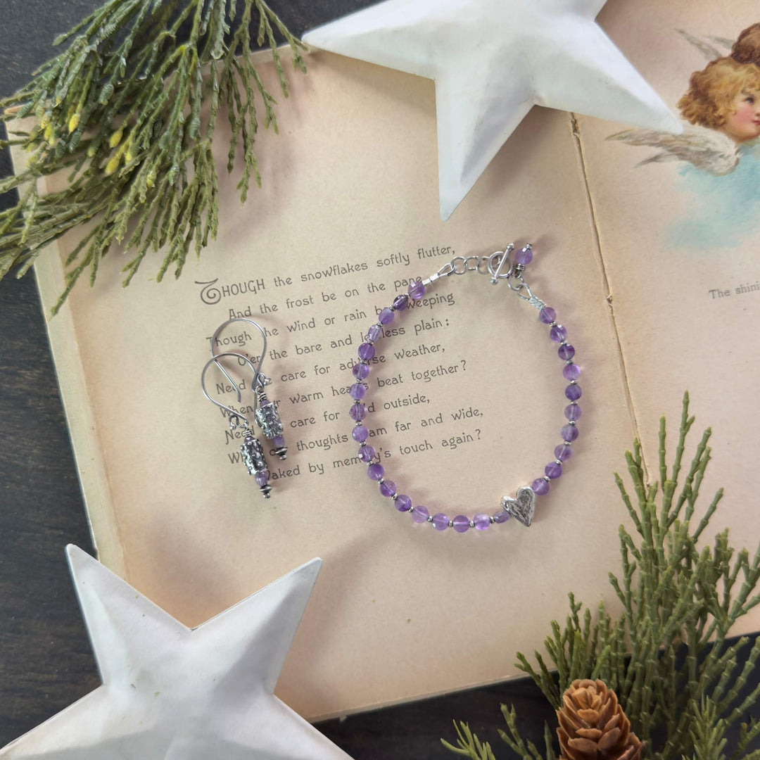 Amethyst bracelet with rustic heart charm and coordinating earrings displayed on a vintage holiday book with greenery and star decor.