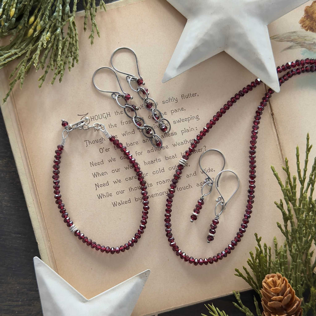Deep garnet necklace, bracelet, and three earring styles with sterling and Thai silver accents on a vintage holiday book with greenery and stars.