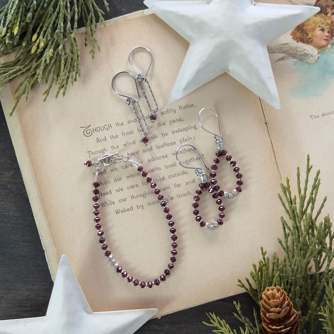 Garnet bracelet and earrings with faceted Thai silver nuggets and oxidized links arranged on a vintage holiday book with greenery and star decor.
