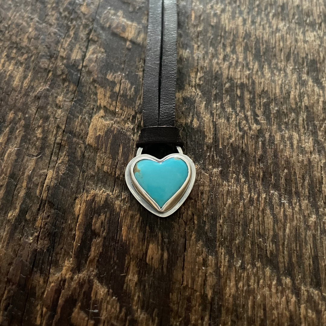 Turquoise heart-shaped pendant on a dark brown cord against a wooden background