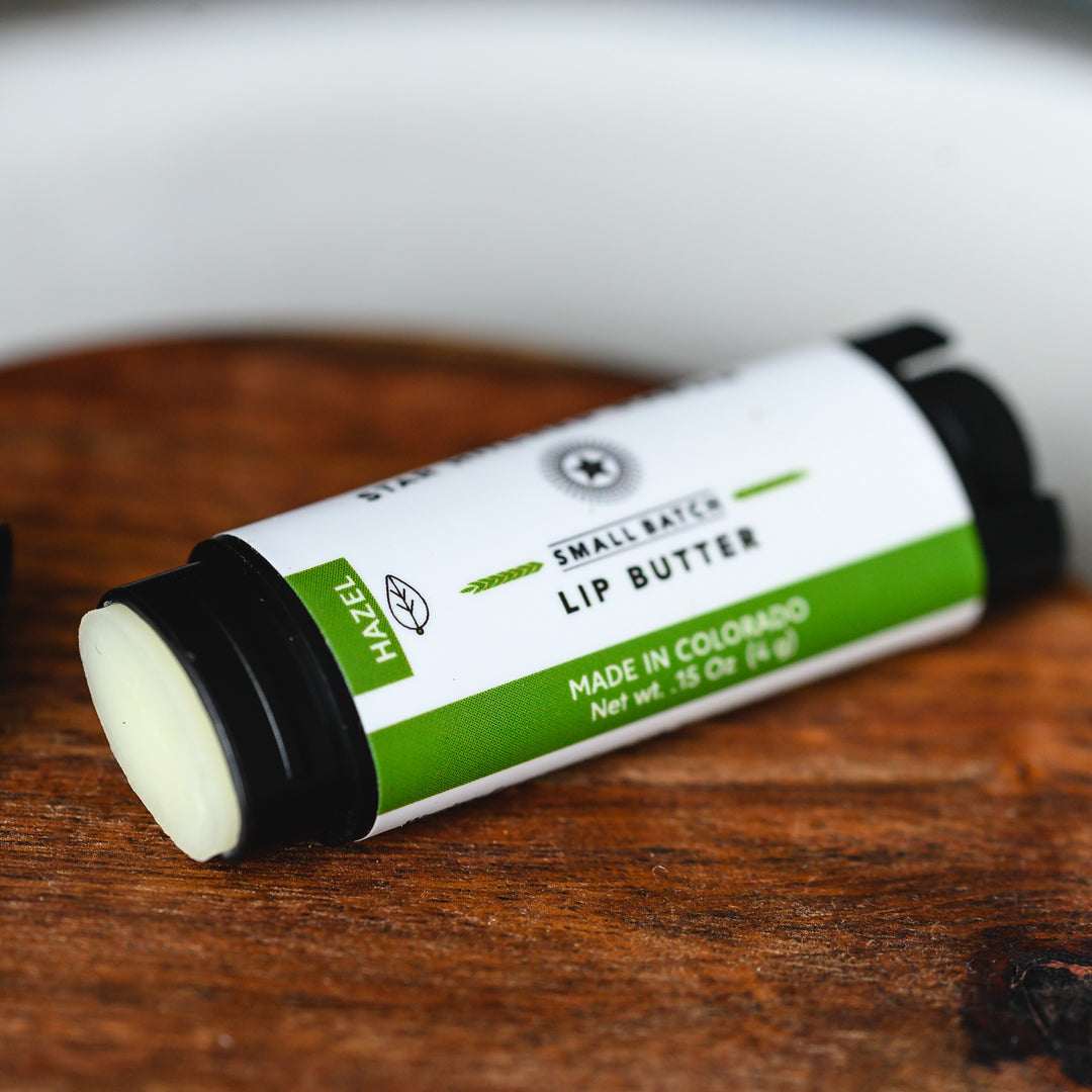 An opened tube of Hazel Lip Butter placed on a wooden surface.